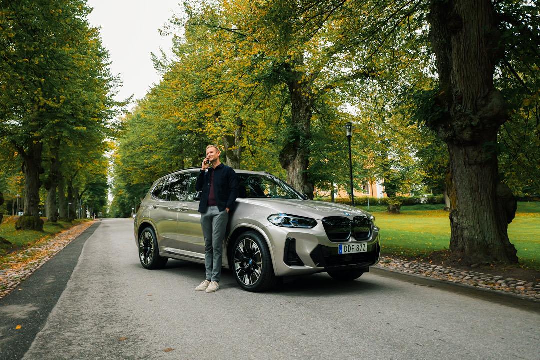 BMW-iX3-Man-pratar-i-telefon-träd-i-bakgrund